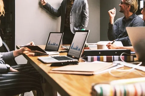 Team members collaborate around a table with laptops during a business meeting.