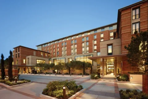 Entrance of a brick lodging building with greenery in the patio area and a blue evening sky
