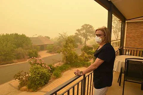 Women with mask stands at balcony overseeing wildfire