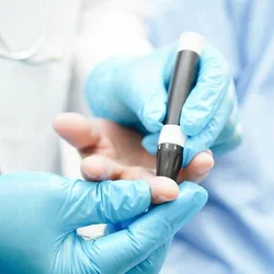 Gloved hands of a doctor use a lancet on a patient's finger to check blood sugar levels.