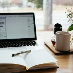 Computer with a mug and journal beside it