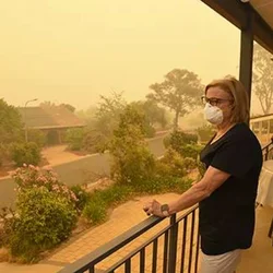 Women with mask stands at balcony overseeing wildfire