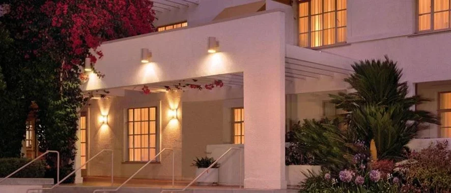 covered overhead porch entrance of a white building with greenery on the sides and stairs leading up